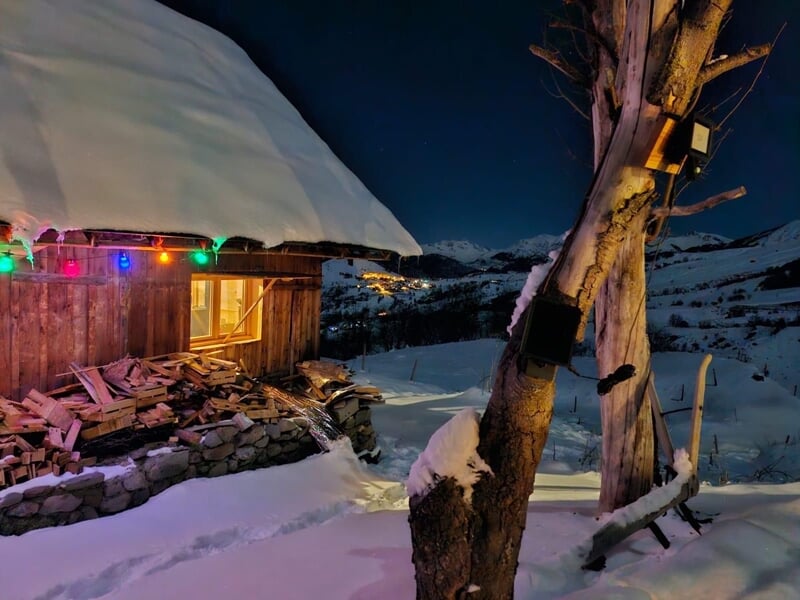 Chalet en bois sous la neige avec lumière intérieure et décorations lumineuses colorées en soirée d'hiver