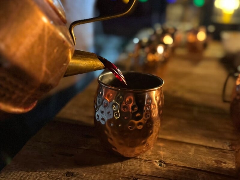 Versement d'une boisson chaude rouge dans une tasse en cuivre sur une table en bois éclairée