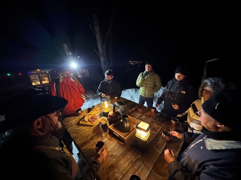 Groupe de personnes habillées chaudement autour d'une table en bois avec lanternes et boissons la nuit