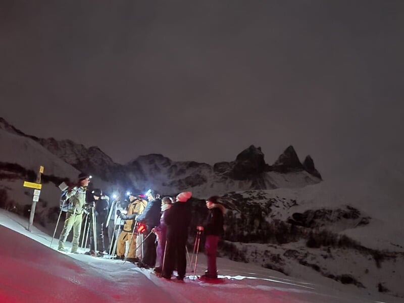 Groupe de randonneurs avec raquettes à neige équipés de lampes frontales en montagne sous un ciel sombre