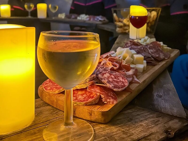 Plan rapproché d'un verre de vin blanc et d'un plateau de charcuterie et fromage sur une table en bois.