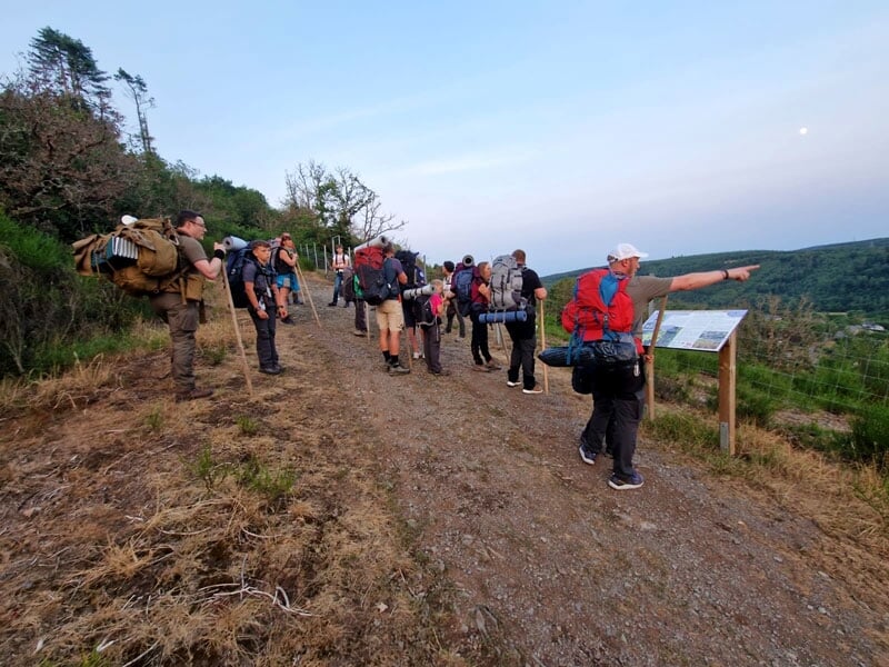 Groupe de randonneurs avec bâtons de marche se reposant sur un sentier de montagne au crépuscule, guidé par un leader pointant au loin