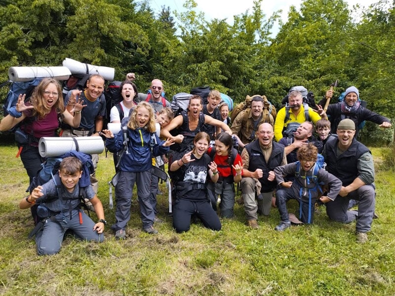 Groupe de randonneurs joyeux et énergiques posant en forêt, souriants et faisant des gestes sauvages vers la caméra