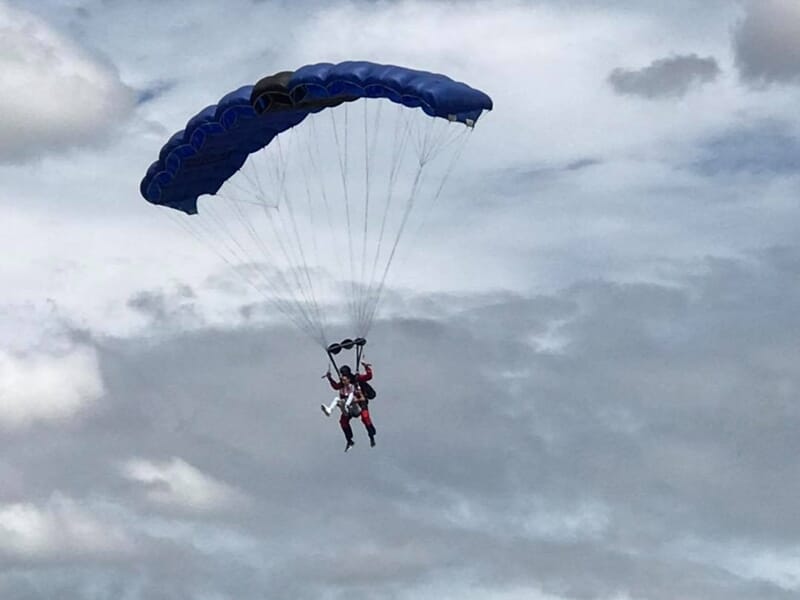 Parachutistes en tandem sous un parachute bleu en descente, ciel nuageux en arrière-plan.