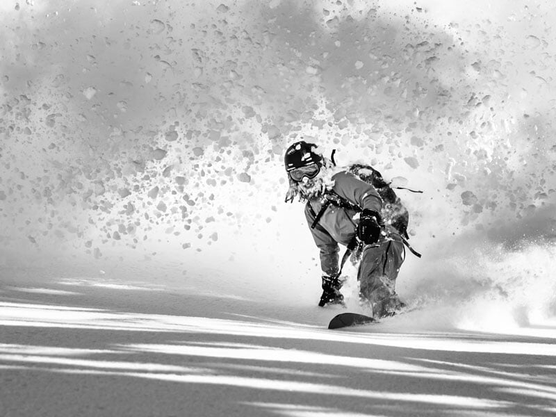 Snowboardeur en action, glissant dans une chute de neige poudreuse, soulevant un nuage de neige derrière lui
