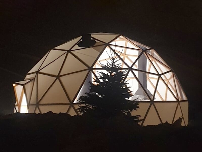 Une vue nocturne d'un dôme éclairé, niché dans un paysage hivernal, offrant un habitat unique et moderne dans un cadre de montagne