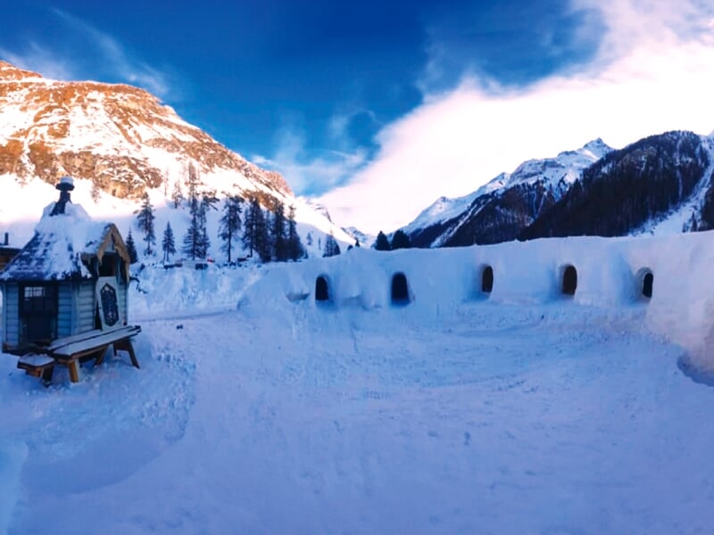 Des montagnes enneigées au coucher du soleil avec un village de dômes de neige et de glace, offrant une ambiance de village hivernal enchanteur
