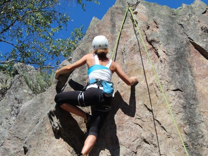 Vue en contreplongée d'une femme grimpant une falaise avec du matériel d'escalade