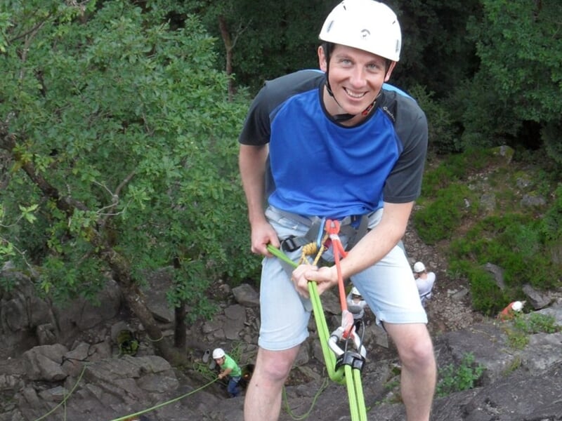 Personne pratiquant la descente en rappel sur une falaise rocheuse au dessus des arbres