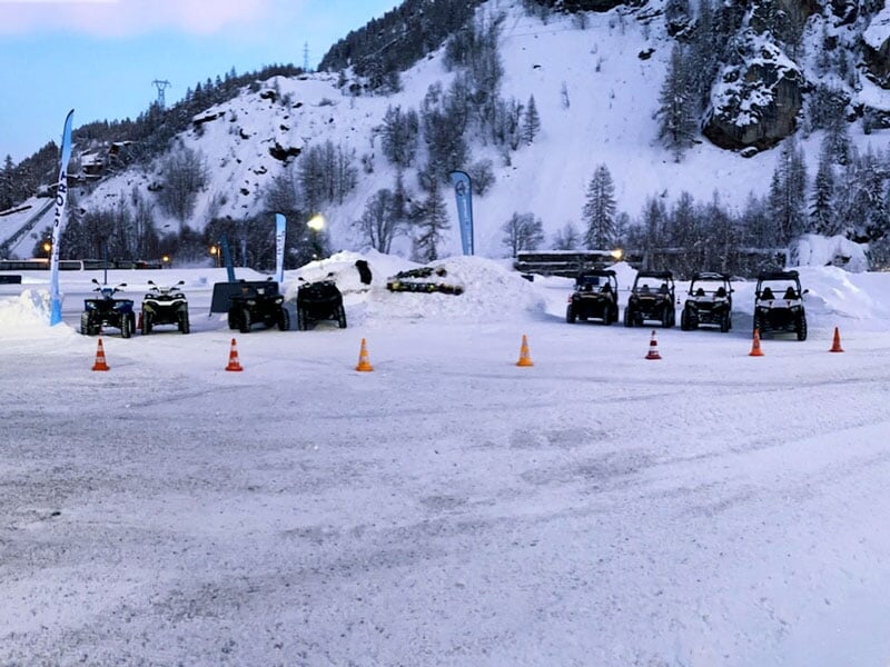 Une série de véhicules tout-terrain noirs alignés sur une piste de glace avec des cônes de signalisation et des montagnes en arrière-plan dans un décor hivernal