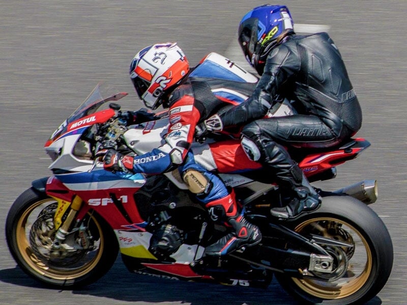 Course de motos sportives avec deux personnes en pleine action sur la piste, sur une Honda rouge et blanche, vue de profil