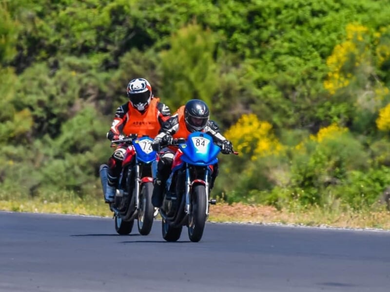 deux personnes en moto de course en ligne droite sur une piste avec de la verdure en arrière plan
