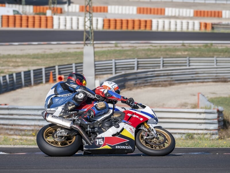 Moto sportive Honda en duo, inclinée dans un virage sur circuit, bordée par des rails de sécurité métalliques