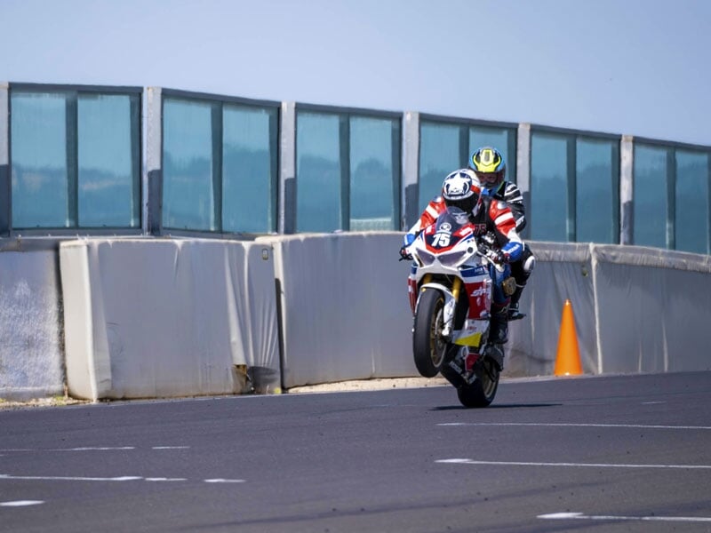 Moto Honda effectuant un wheeling sur la ligne droite d’un circuit, avec pilote et passager en pleine accélération