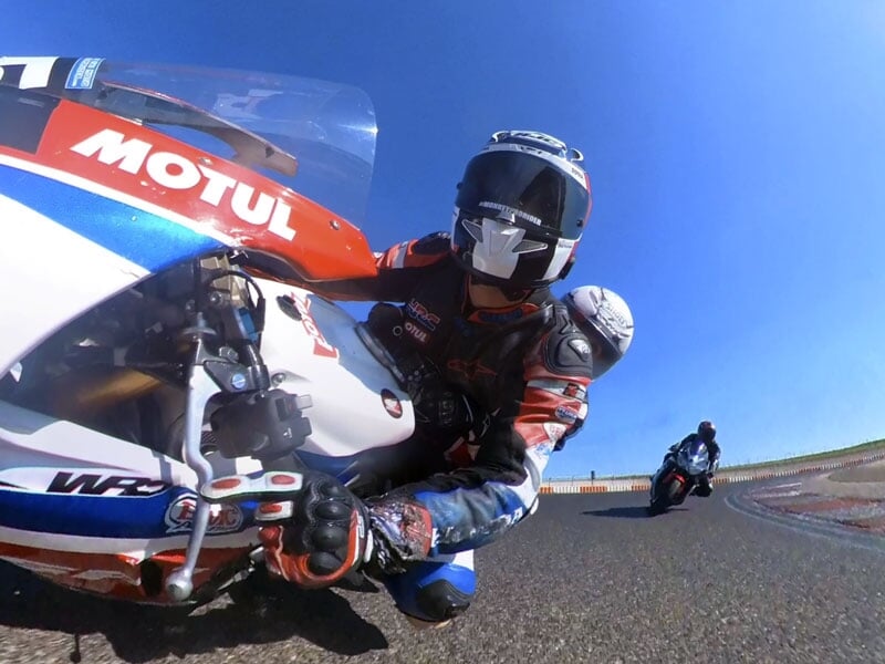 Gros plan dynamique d’un motard et son passager penchés dans un virage, sur une piste de course en plein soleil