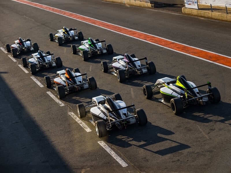 Alignement de monoplaces de course blanches avec des accents de couleurs différentes, sur la ligne de départ d'un circuit automobile