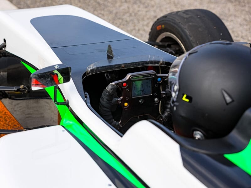 Vue rapprochée du cockpit d'une monoplace avec volant de course, écran de données et détails verts sur la carrosserie.