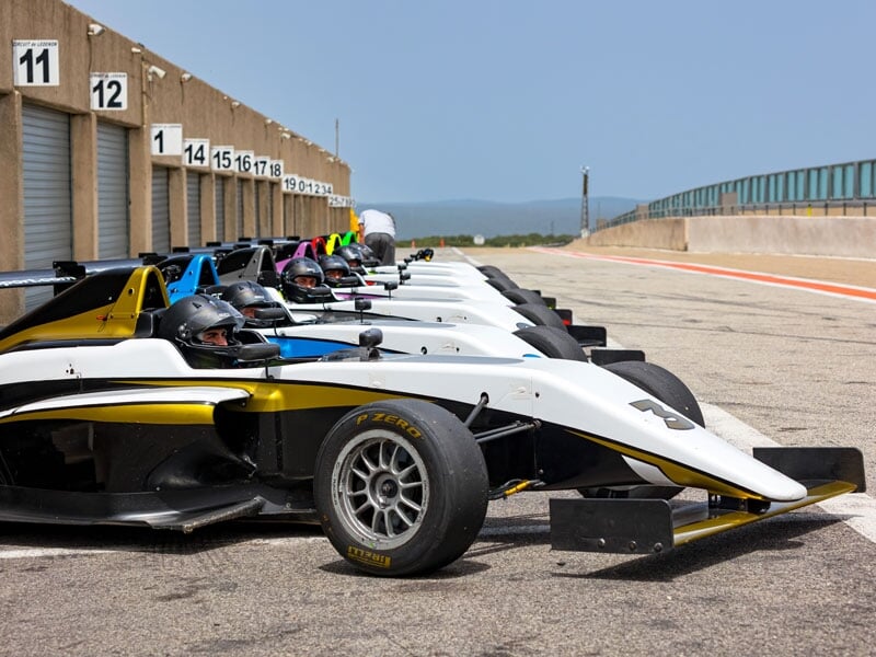 Monoplaces de course alignées sur la ligne des stands d'un circuit, prêtes pour un stage de pilotage de formule 4