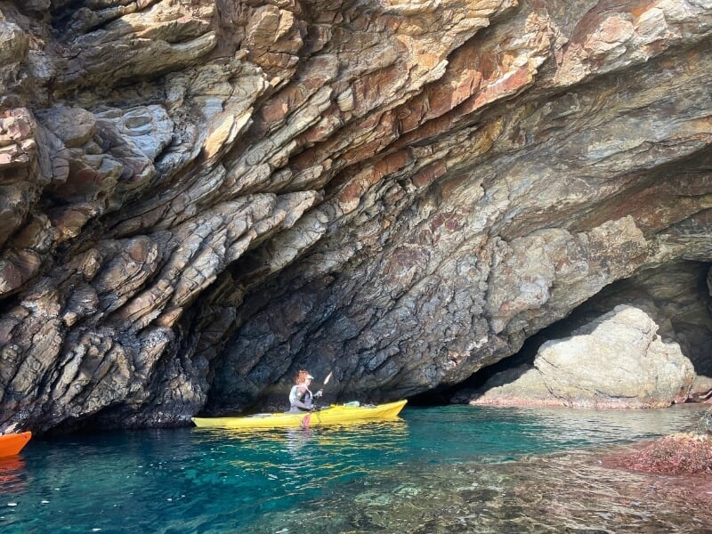 Kayakiste solitaire naviguant près d'une grotte dans une falaise rocheuse avec des eaux turquoise, évoquant l'aventure et l'exploration