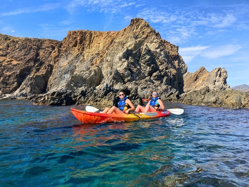 Côte martime, deux kayakistes sur un kayak double prennent la pose devant les roches.