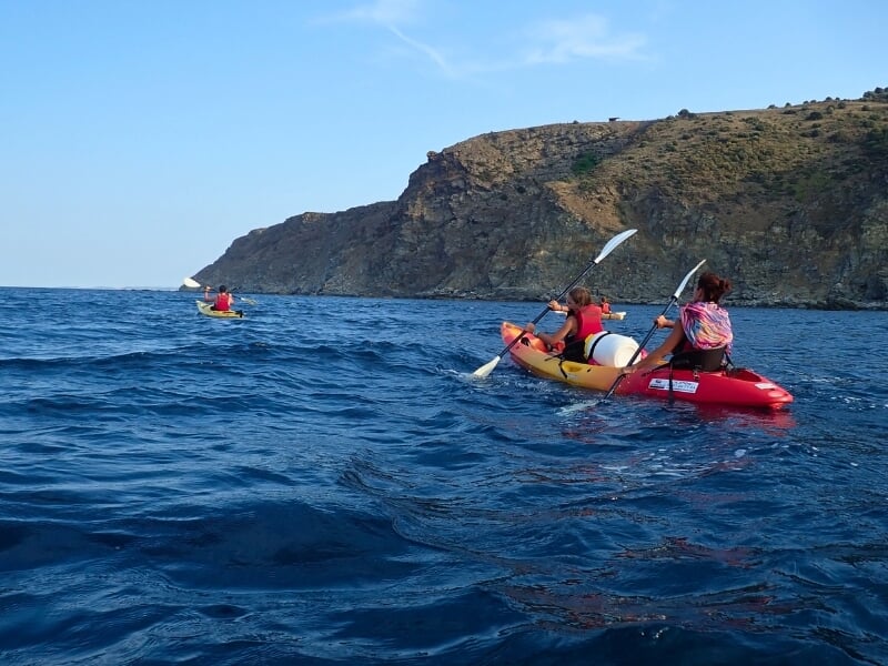 Deux kayaks, un simple en arrière plan et un double au premier plan. A leur bord des kayakistes. Ils voguent sur une mer calme.