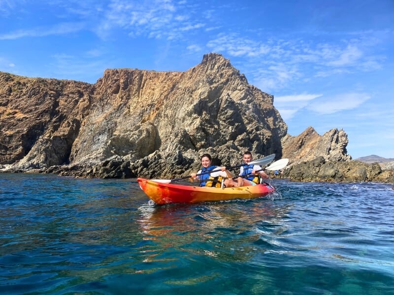 Devant des roches claires, deux kayakistes pagaient dans la même embarcation.
