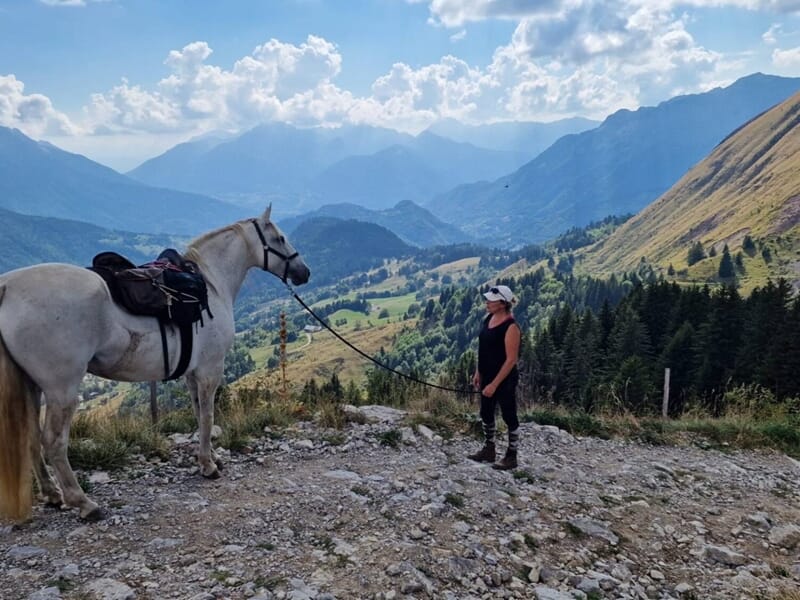 personne à côté d'un cheval scellé profitant du panorama de la montagne en arrière plan