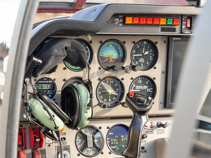 Tableau de bord d'un avion avec plusieurs instruments analogiques, un casque posé sur le côté et un manche à balai au premier plan.