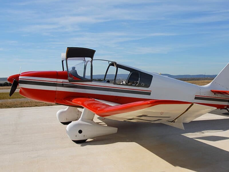 Avion de sport blanc et rouge garé sur une piste en béton sous un ciel clair.