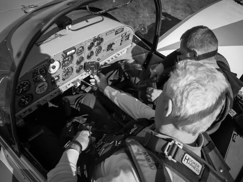 Deux pilotes à l'intérieur du cockpit d'un avion de voltige, ajustant les commandes et vérifiant les instruments de bord. Scène en noir et blanc mettant en avant la concentration et la préparation ava
