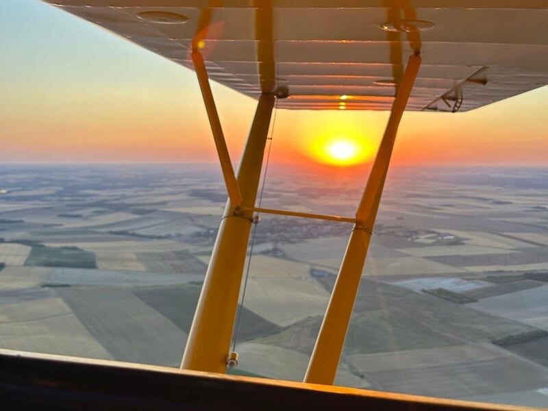 Vue depuis l'intérieur d'un avion léger au coucher du soleil avec un paysage de champs à perte de vue.