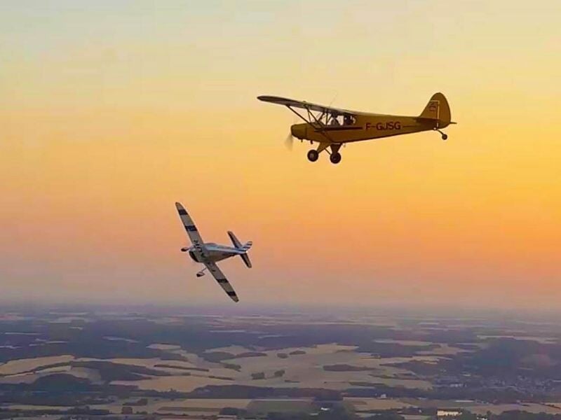 Deux avions légers volant dans un ciel aux couleurs chaudes du coucher de soleil au-dessus de la campagne.