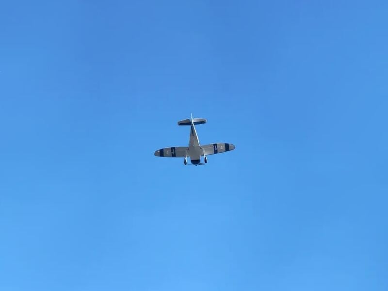 Vue d'un petit avion blanc vu de dessous en plein vol dans un ciel bleu clair sans nuages.