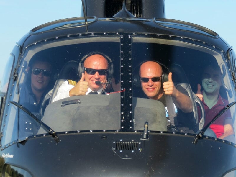 des personnes font un signe de la main depuis le cockpit de l'hélico AS350