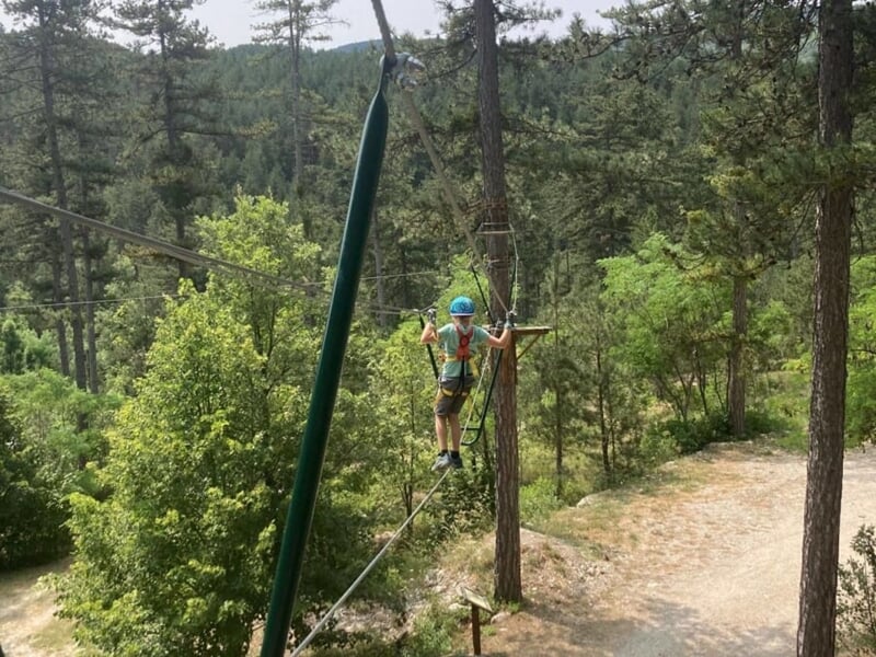 enfant pratiquant l'accrobranche en équilibre sur une corde en forêt