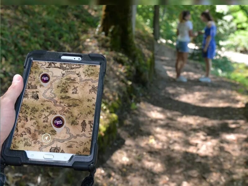personne tenant une tablette tactile affichant une carte pour la réalisation d'un escape game en pleine nature