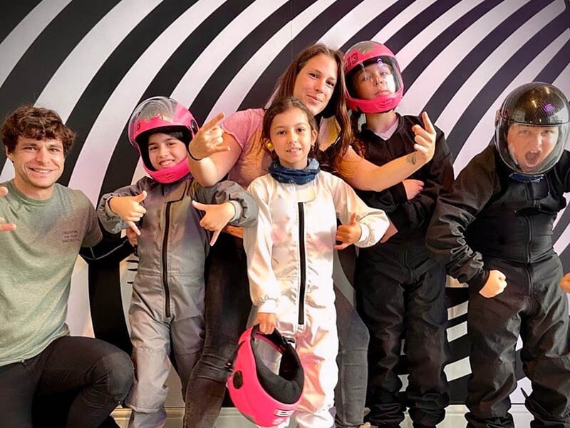Un groupe de personnes en combinaisons de vol posant pour une photo devant un mur à rayures dans un centre de chute libre intérieur
