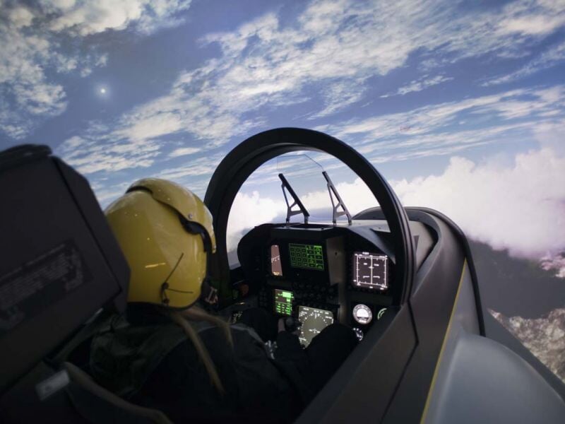 Vue depuis un simulateur de pilotage d'avion avec un casque jaune et un ciel nuageux visible à travers le cockpit.