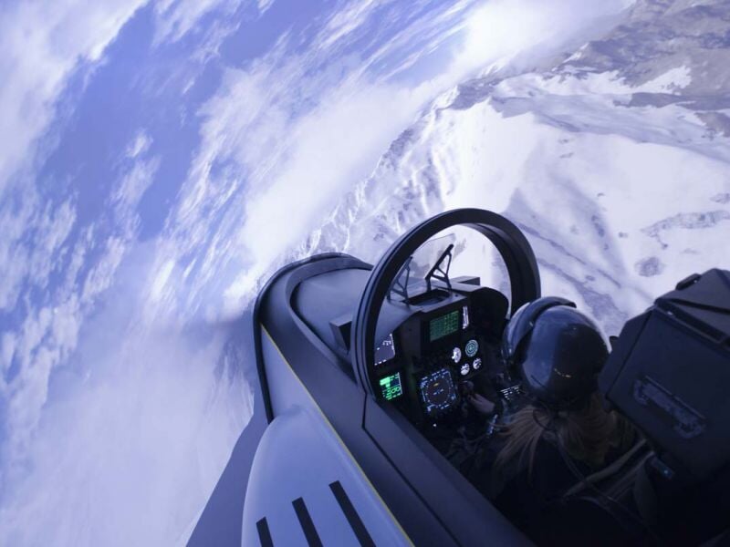 Personne avec casque noir dans un simulateur d'avion effectuant une manœuvre avec vue sur un ciel nuageux incliné.