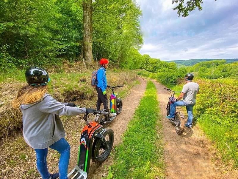 Trois personnes en balade sur un chemin de campagne avec des trottinettes électriques dans un paysage verdoyant et boisé, lors d'une randonnée dans le Morvan.
