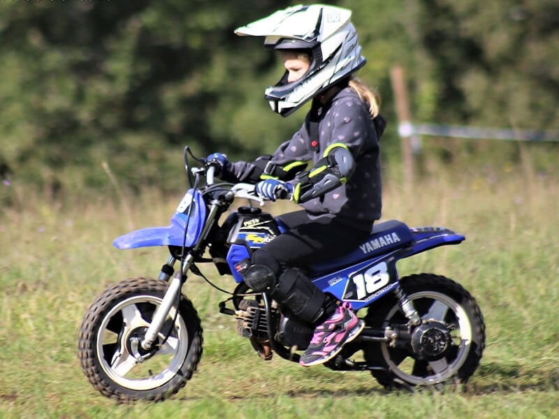 Enfant pilotant une mini-moto Yamaha bleue, équipement de protection complet, concentré sur une piste herbeuse