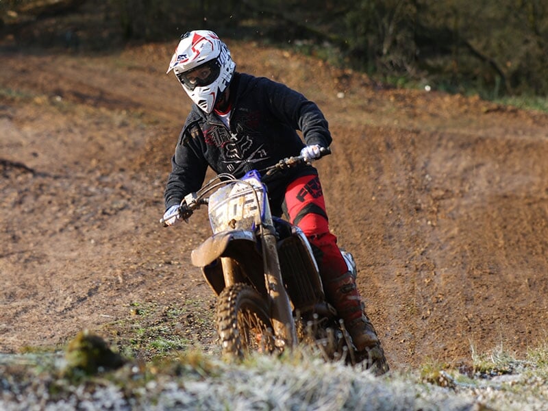 Motocross en hiver, pilote en noir et rouge sur une piste givrée, lumière matinale, foret enneigée en arrière-plan, ambiance froide