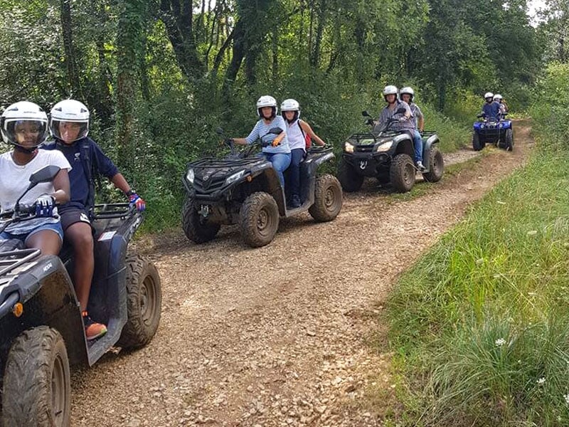 Groupe de personnes pratiquant le quad en sentier forestier, casques de sécurité blancs, quads couverts de boue