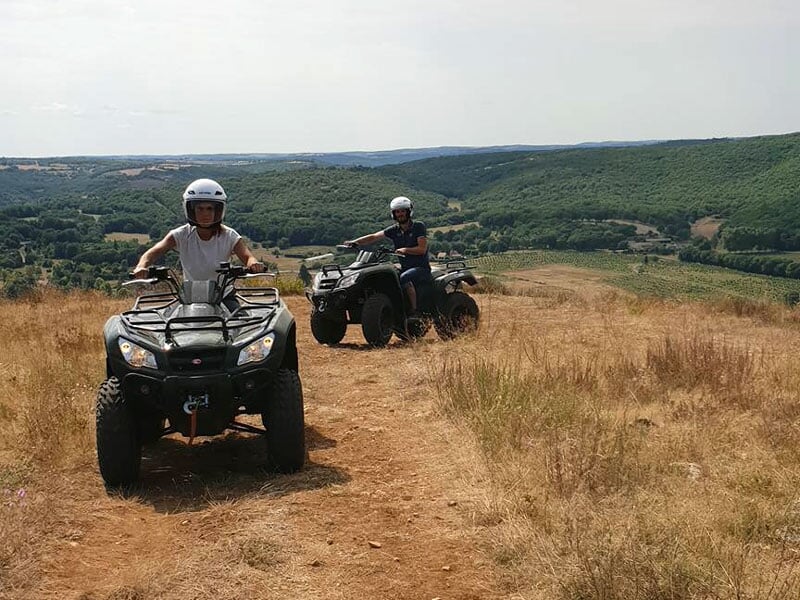 Expédition en quad surplombant un paysage vallonné, ciel légèrement nuageux, végétation sèche au premier plan