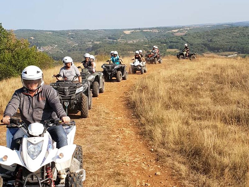 File de quads en randonnée, casques variés, sentier herbeux avec horizon dégagé.