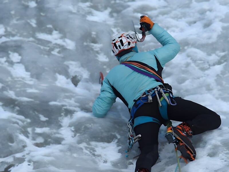 Un grimpeur en tenue d'escalade sur glace avec piolet et crampons, grimpant une paroi glacée.