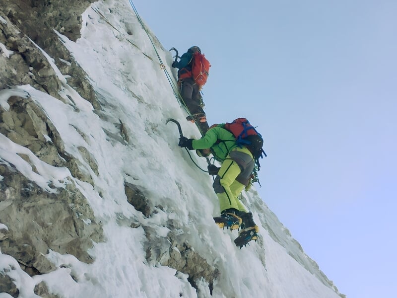 Deux alpinistes en équipement d'escalade complet grimpant une paroi glacée, le premier en rouge et le deuxième en vert, tous deux attachés à des cordes de sécurité