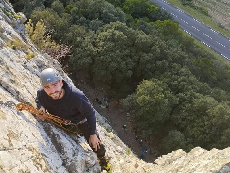 homme grimpant une falaise au dessus des arbres