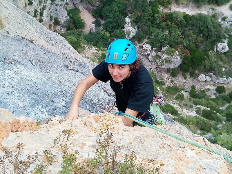 une personne vue du dessus escalade une paroi de pierre avec un casque d'escalade
