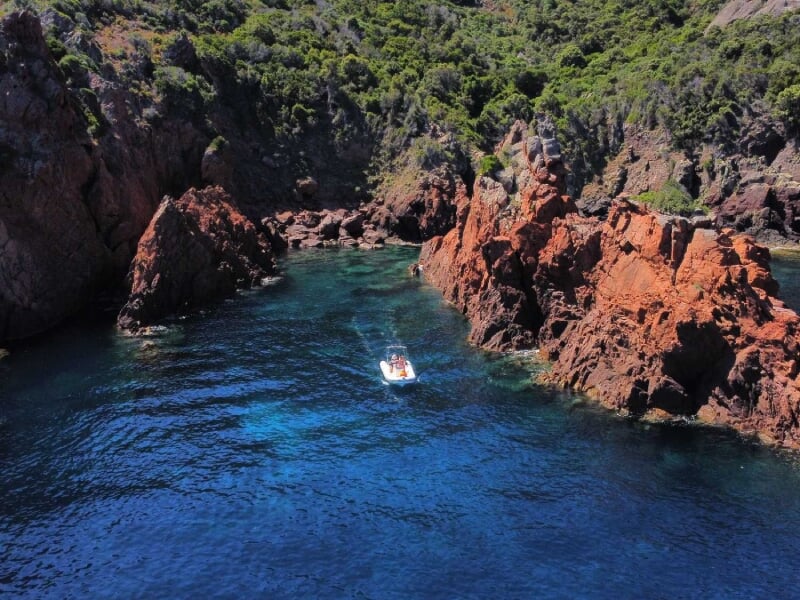 Petit bateau naviguant entre des falaises rougeâtres et des eaux bleu profond entourées de verdure luxuriante.